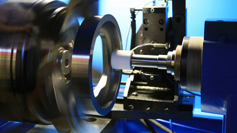 Close-up of a precision grinding machine shaping a rotating metal part, showing high-speed motion and tooling used in advanced manufacturing.