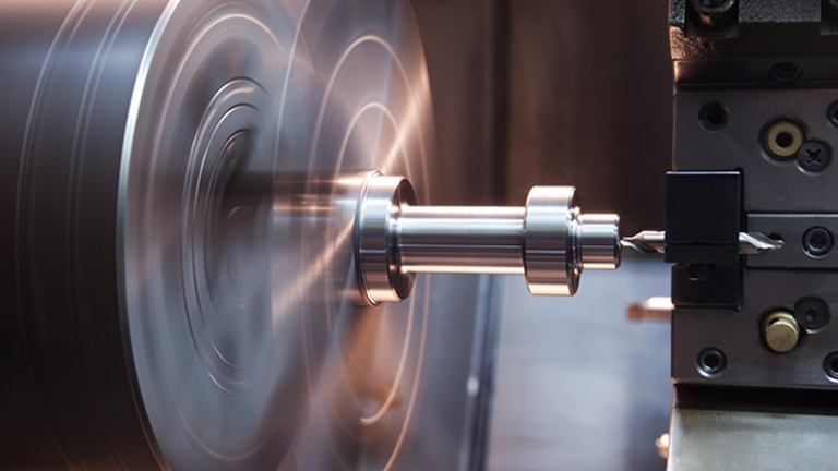A CNC lathe machine in operation, rotating a metal workpiece at high speed while a cutting tool shapes its surface with precision.