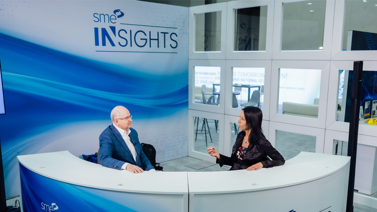 Jeannine Kunz, CEO of SME, sits behind an anchor desk with Greg Jones at the SME Insights booth at Mission Critical