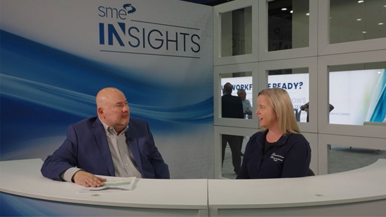 Amy Stage from the Real Life Rosies program sits behind a white desk and interviews with SME at the SME Insights booth