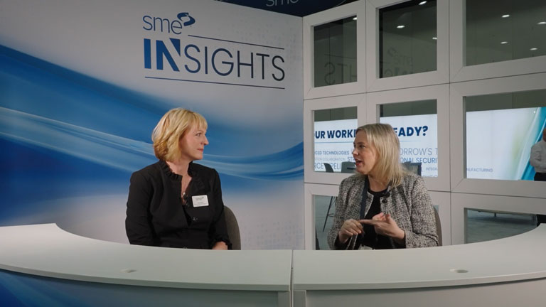 Tara May from Aspiritech sits behind a white desk and interviews with SME at the SME Insights booth and discusses neurodiversity in manufacturing