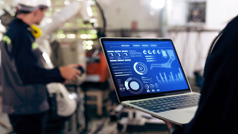 A laptop screen with a manufacturing worker in the background
